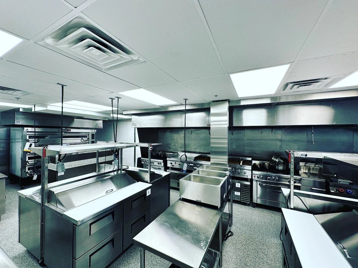 Wide finished commercial kitchen with cook line, hoods, and prep islands